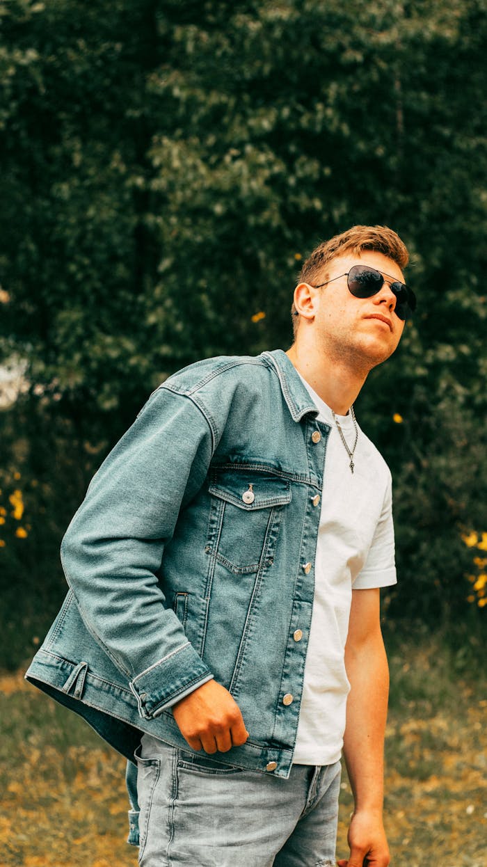 Stylish outdoor portrait of a young man in sunglasses and a jean jacket, exuding confidence.